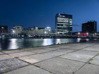 some very pretty tall buildings by the water at night time, taken from near the river