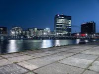 some very pretty tall buildings by the water at night time, taken from near the river