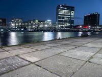 some very pretty tall buildings by the water at night time, taken from near the river