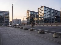 some concrete bollarps along side of an empty street on a sunny day and buildings in the background