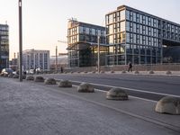 some concrete bollarps along side of an empty street on a sunny day and buildings in the background