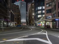 an empty city street at night with lights in the buildings around and painted lines on the sidewalk