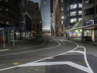 an empty city street at night with lights in the buildings around and painted lines on the sidewalk