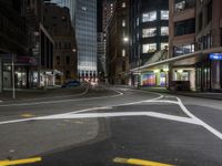 an empty city street at night with lights in the buildings around and painted lines on the sidewalk