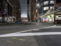 an empty city street at night with lights in the buildings around and painted lines on the sidewalk