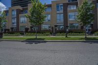 a tall building with lots of windows, trees and grass on the side of the road