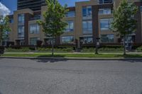 a tall building with lots of windows, trees and grass on the side of the road