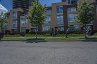 a tall building with lots of windows, trees and grass on the side of the road