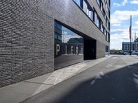 a city street that is empty with buildings reflected in the windows of it behind a brick wall