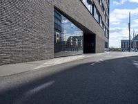 a city street that is empty with buildings reflected in the windows of it behind a brick wall