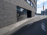 a city street that is empty with buildings reflected in the windows of it behind a brick wall