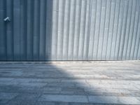 a street light sitting next to a large wall on a brick floor next to a parking meter