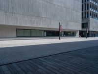 a black traffic light on the sidewalk next to an empty sidewalk with a concrete building