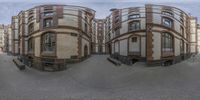 two buildings are seen through the same fisheye lens in this image, there is a bench to go on the sidewalk