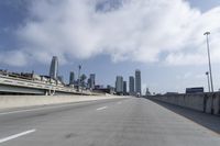 empty highway running over overpasss with highrise buildings in the distance and a blue sky above