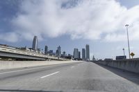 empty highway running over overpasss with highrise buildings in the distance and a blue sky above