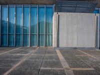 a sidewalk that has several glass doors next to it with buildings in the background behind