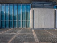 a sidewalk that has several glass doors next to it with buildings in the background behind