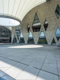 large concrete building with curved glass windowed roof, outside view, and open walkway