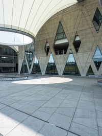 large concrete building with curved glass windowed roof, outside view, and open walkway