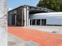 a brick walkway that is next to a building with a round metal structure and two large white circular white containers