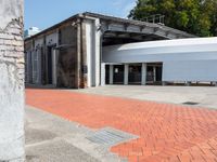 a brick walkway that is next to a building with a round metal structure and two large white circular white containers