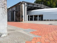 a brick walkway that is next to a building with a round metal structure and two large white circular white containers