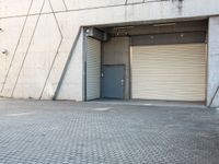 an empty, open garage with several rolling up doors on the side walk between brick pavement