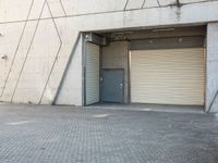 an empty, open garage with several rolling up doors on the side walk between brick pavement