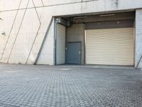 an empty, open garage with several rolling up doors on the side walk between brick pavement