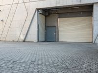 an empty, open garage with several rolling up doors on the side walk between brick pavement