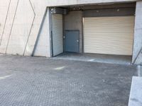 an empty, open garage with several rolling up doors on the side walk between brick pavement