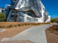 a modern architectural building made out of large pieces of metallic and silver, in front of blue skies