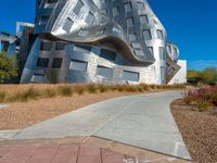 a modern architectural building made out of large pieces of metallic and silver, in front of blue skies