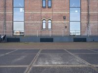 the building has windows near the concrete floor with an empty parking lot outside it and a motorcycle parked beside the window