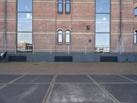 the building has windows near the concrete floor with an empty parking lot outside it and a motorcycle parked beside the window