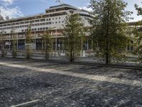 a picture of a large building in the background with people walking around it and some trees