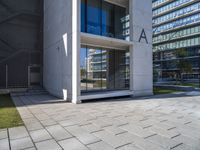 a modern office building surrounded by grass and stone tiles on the outside of it and an external door to the entrance