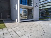 a modern office building surrounded by grass and stone tiles on the outside of it and an external door to the entrance