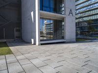 a modern office building surrounded by grass and stone tiles on the outside of it and an external door to the entrance