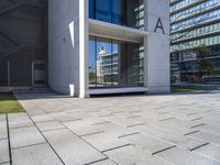 a modern office building surrounded by grass and stone tiles on the outside of it and an external door to the entrance