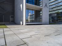 a modern office building surrounded by grass and stone tiles on the outside of it and an external door to the entrance