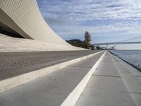 an empty concrete walkway that is surrounded by stone steps and a bridge in the distance