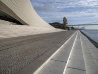 an empty concrete walkway that is surrounded by stone steps and a bridge in the distance