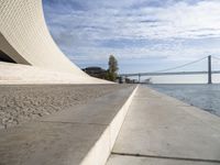 an empty concrete walkway that is surrounded by stone steps and a bridge in the distance