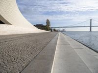 an empty concrete walkway that is surrounded by stone steps and a bridge in the distance