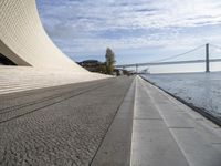 an empty concrete walkway that is surrounded by stone steps and a bridge in the distance