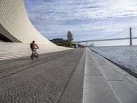 an empty concrete walkway that is surrounded by stone steps and a bridge in the distance