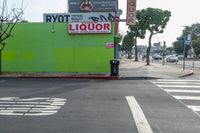 an intersection with signs and advertisements, as well as buildings and trees, near a crosswalk