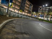 the asphalted road is empty outside the building at night, with parking spaces at the curb